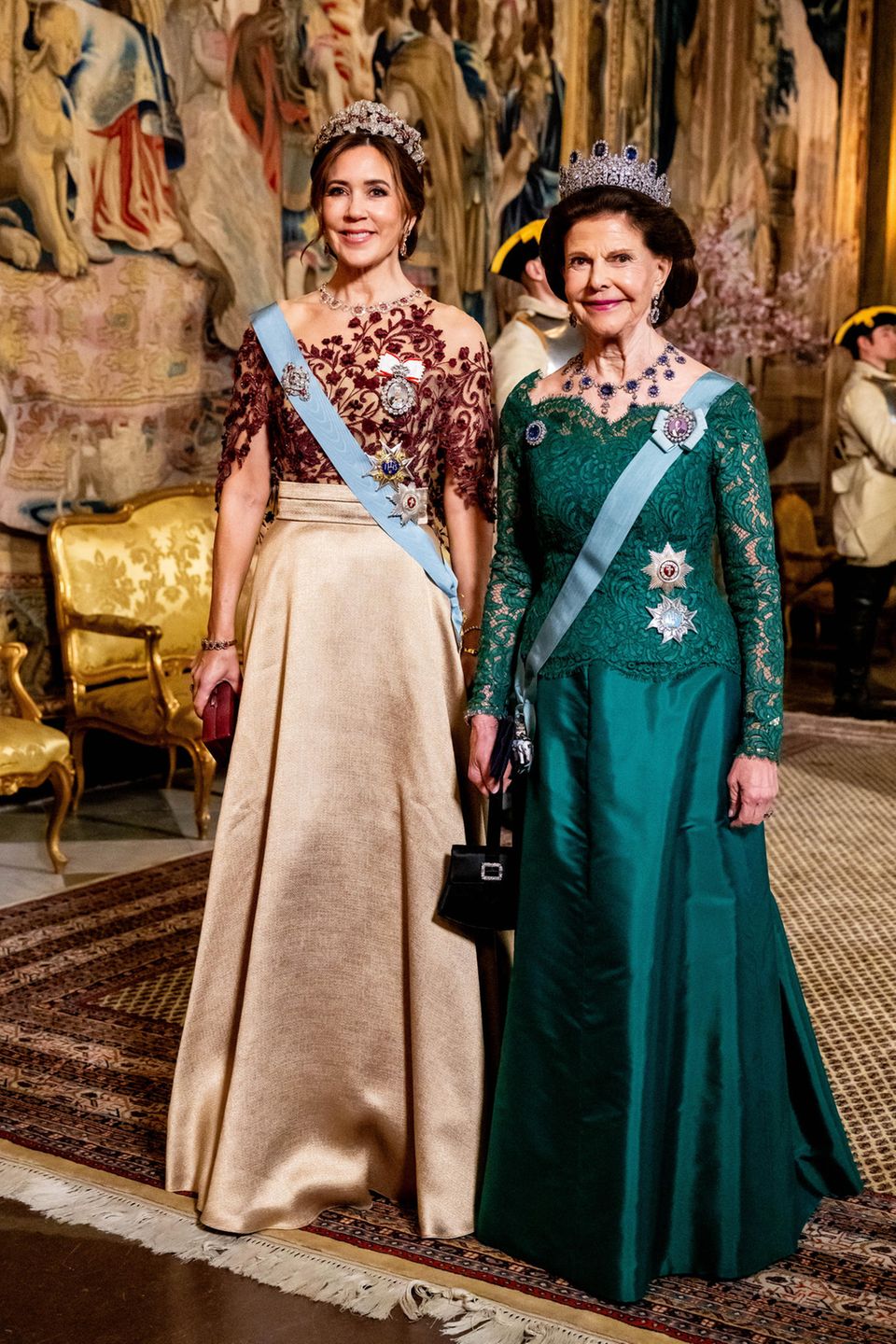 Beim Staatsbankett in Schweden, zu Ehren des dänischen Königspaares, strahlen Königin Mary und Königin Silvia in ihren prächtigen Roben. Als Ehrengästin trägt Königin Mary einen goldenen Seidenrock, den sie mit einem Oberteil aus rubinroten Verzierungen kombiniert. Passend zum Rubinrot verziert die Ruby Parure Tiara das Haupt der dänischen Königin und verpasst ihr ein majestätisches Auftreten. Königin Silvia hingegen glänzt in einem smaragdgrünen Spitzenkleid von "Georg et Arend", das sie elegant mit blauen Saphiren in ihrer Leuchtenberg-Saphir-Tiara und ihrem Halsschmuck kombiniert. Beide Königinnen verkörpern nicht nur Eleganz, sondern auch die wertvollen Verbindungen zwischen ihren Nationen, was die Pracht dieses besonderen Anlasses unterstreicht.
