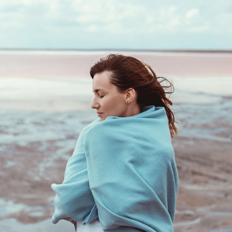 Psychologie: Eine müde Frau in einer Decke am Strand