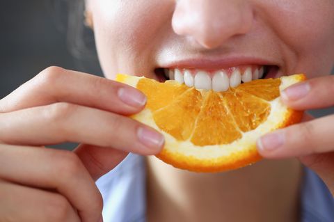 Eine junge Frau beißt in eine Orangenscheibe