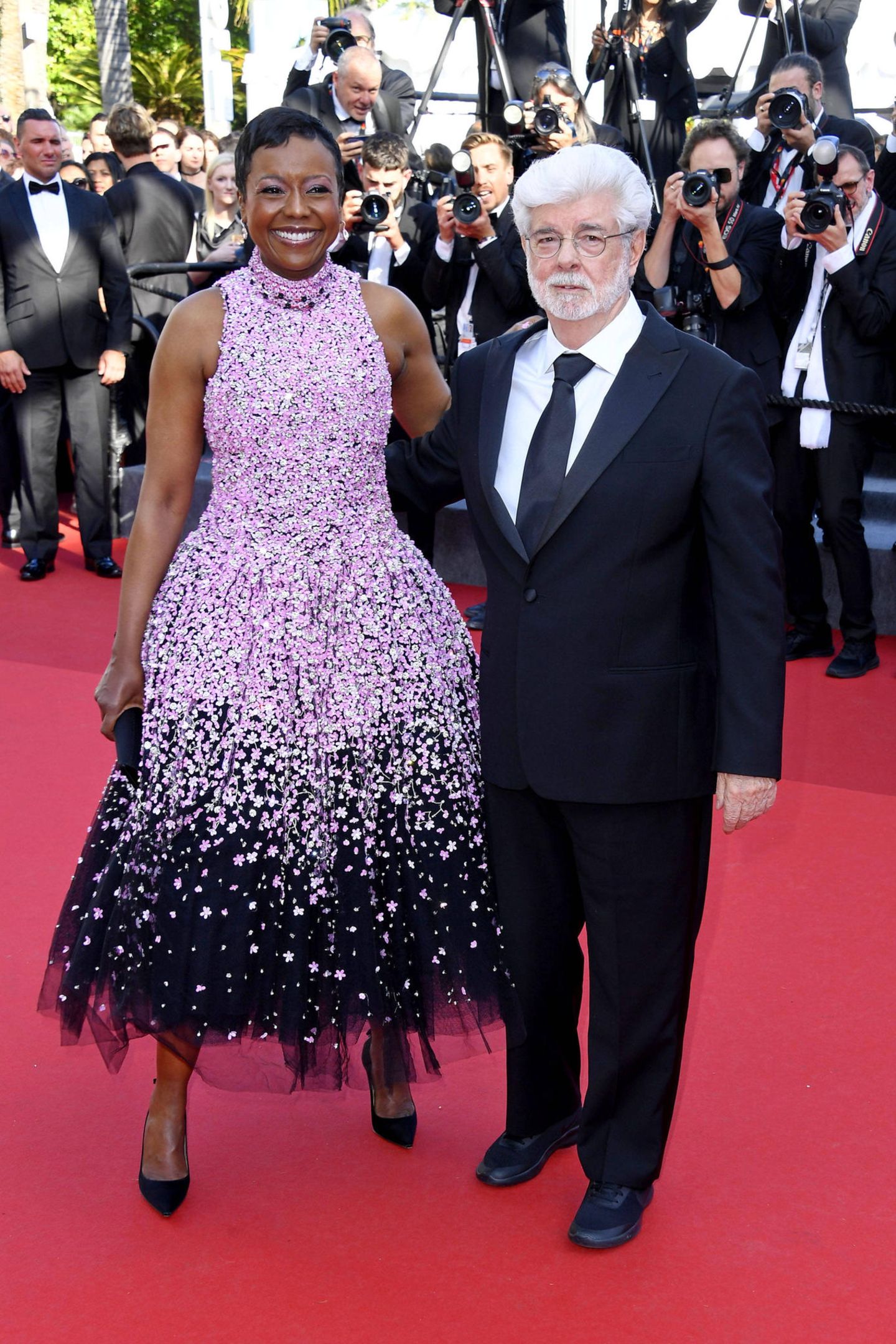 George Lucas hält seine Frau Mellody Hobson im Kirschblüten-Dress mit schwarzem Tüllrock von Richard Quinn im Arm.
