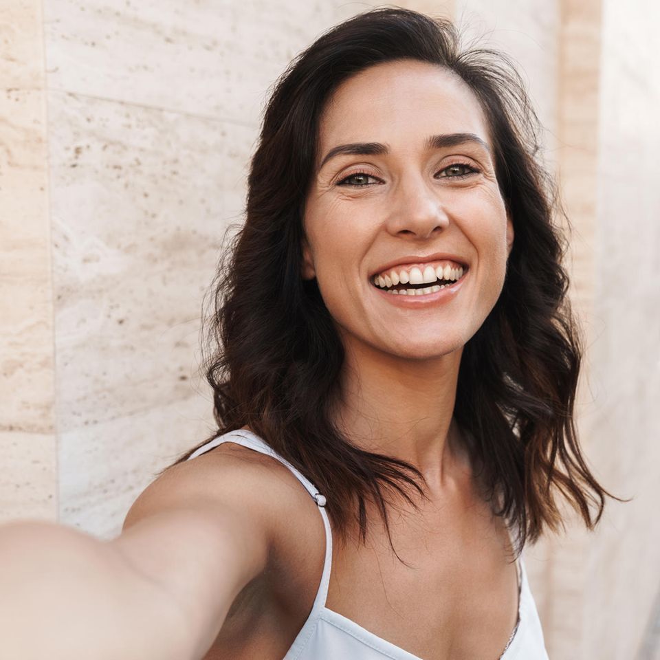 Frisur ab 40: Eine Frau mit dunklen Haaren lächelt frontal in die Kamera