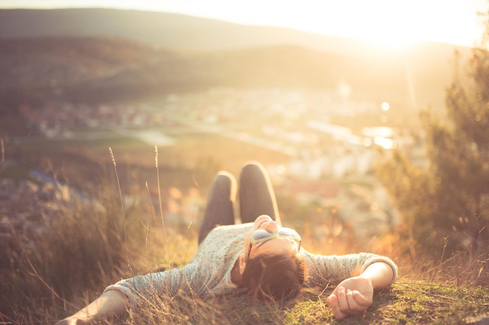 Wochenend-Horoskop ab 7.6.: Eine Frau liegt auf einem Hügel in der Sonne