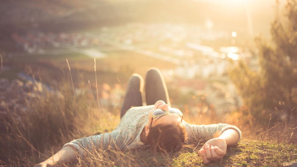 Wochenend-Horoskop ab 7.6.: Eine Frau liegt auf einem Hügel in der Sonne