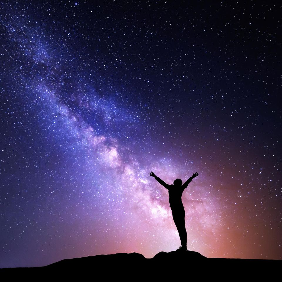 Silhouette einer Frau, die auf einem Stein steht, umgeben von Sternen und der Milchstraße am Nachthimmel