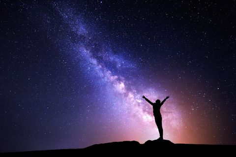 Silhouette einer Frau, die auf einem Stein steht, umgeben von Sternen und der Milchstraße am Nachthimmel