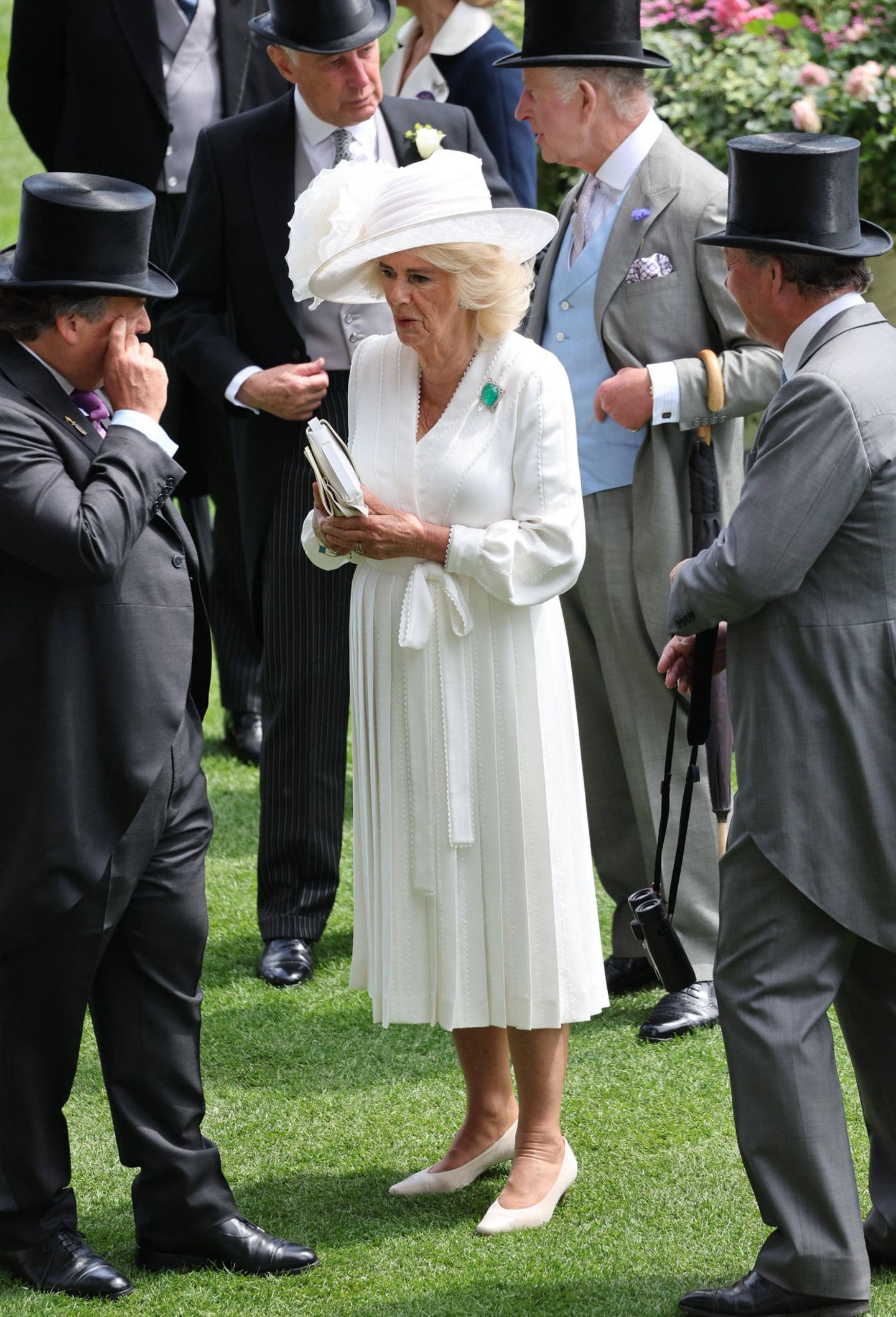 Zwar ist Camilla am Ladies Day in Ascot umringt von Gentlemen, im weißen Seiden-Dress mit Faltenrock von Dior und passendem Hut von Philip Treacy sticht die Königin aber ganz klar hervor. Ein farblich schöner Hingucker ist hier auch die Delhi-Smaragd-Brosche von Queen Mary.