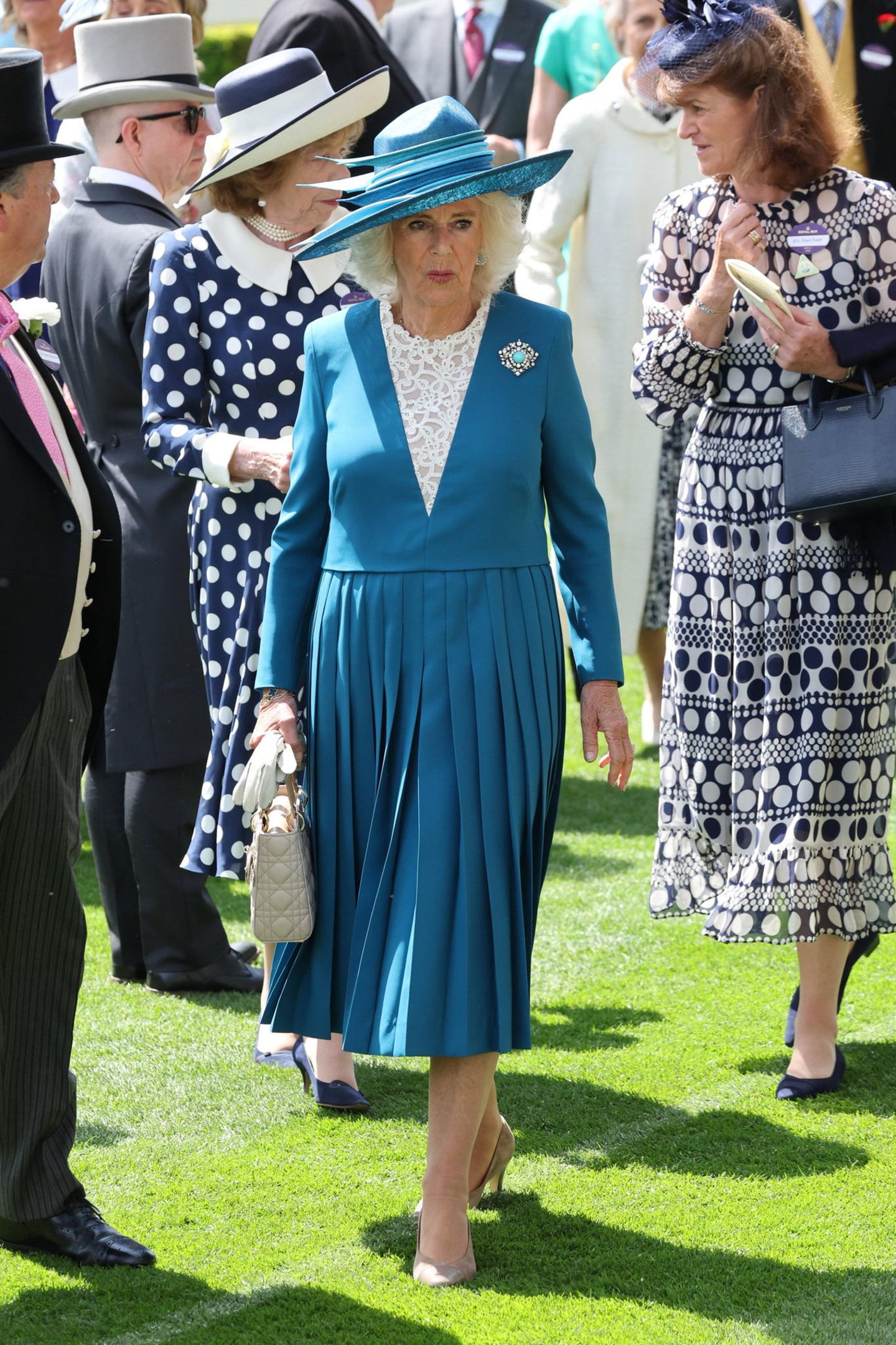 Im matt azurblauen Faltenrock-Dress mit weißer Spitze zeigt sich Königin Camilla am ersten Tag des diesjährigen Pferderennens in Ascot.