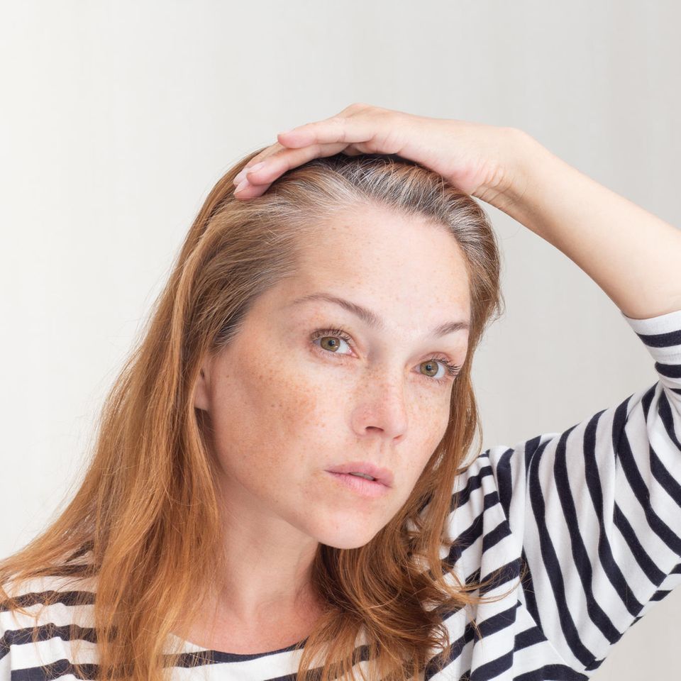 Graue Haare: Eine guckt sich ihren grauen Haaransatz im Spiegel an