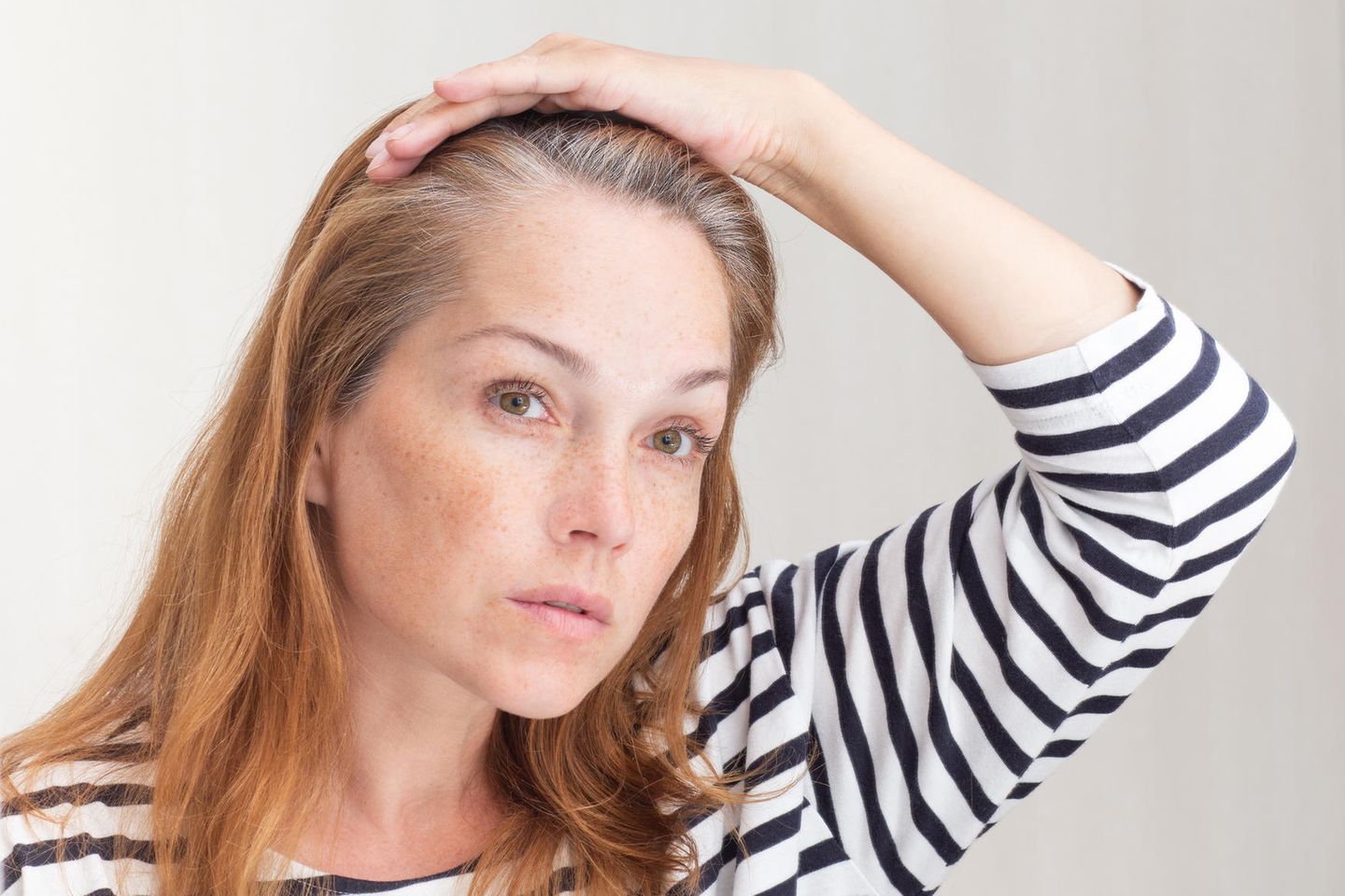 Graue Haare: Eine guckt sich ihren grauen Haaransatz im Spiegel an