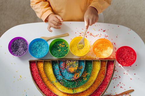 Geschlechtsoffene Erziehung: Kind spielt mit regenbogenbuntem Reis 1.5004