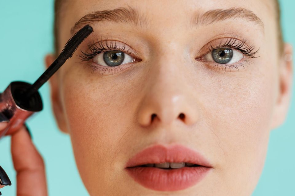 Woman applies tubing mascara to her eyelashes.