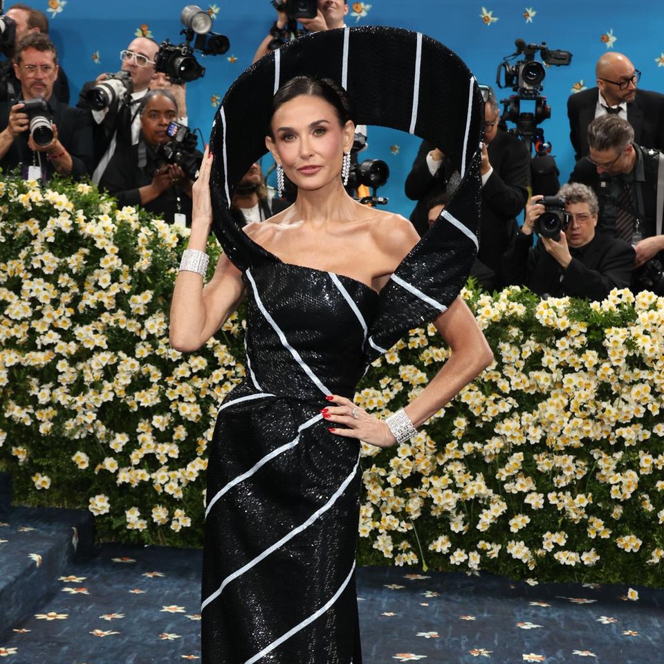 Demi Moore posiert auf dem blauen Teppich in einer besonderen Robe von Thom Browne, dessen besonderes Dekolleté-Detail ihr Gesicht rahmt. 