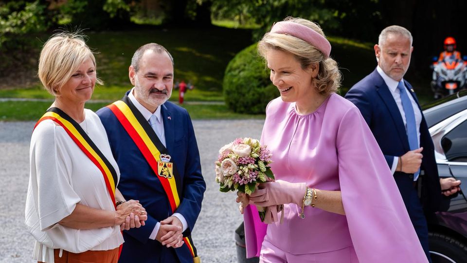 Königin Mathilde von Belgien macht in einem lila-rosa Cape vor, wie man die Lieblingsfarbe der Royals im Sommer 2025 trägt. 