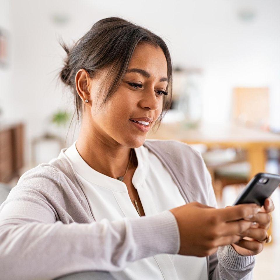 Eine dunkelhaarige Frau schaut neugierig auf ihr Smartphone