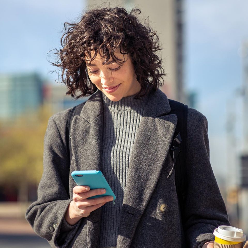Frau schaut draußen auf ihr Handy: Um diese Uhrzeit haben wir die besten Chancen auf Erfolg