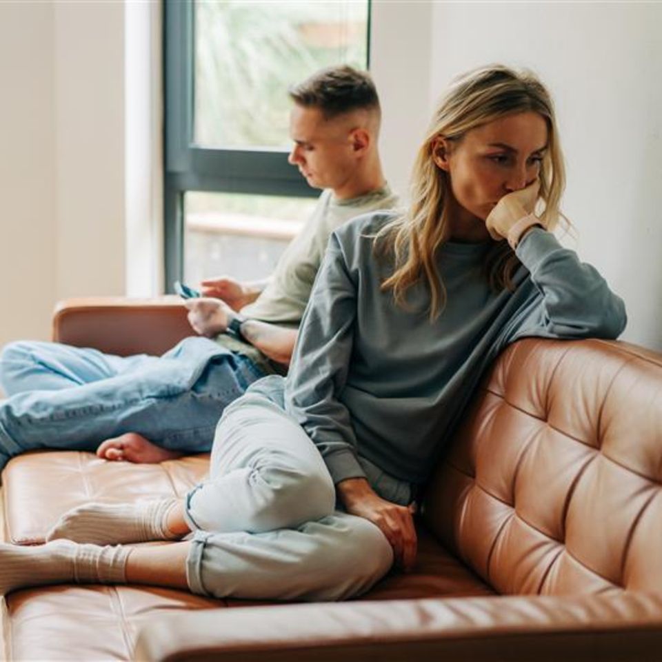 Eine Frau sitzt von ihrem Partner abgewendet auf dem Sofa.