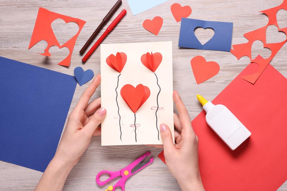 Valentinstagskarte basteln: Hände halten selbst gebastelte Karte mit 3D-Herzballons-Motiv