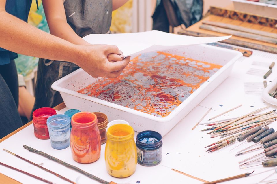 Marmorieren: Erwachsener und Kind legen gemeinsam Papier in Farbwanne