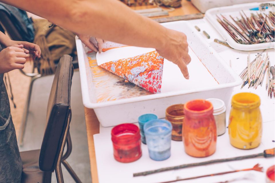 Marmorieren: Marmoriertes Papier wird aus Farbwanne gehoben