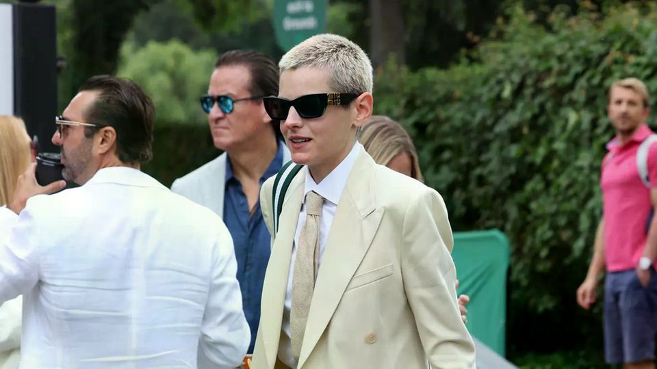 Emma Corrin glänzt im Anzug-Style mit Karwatte. Für etwas Bruch sorgt die große Sonnenbrille.