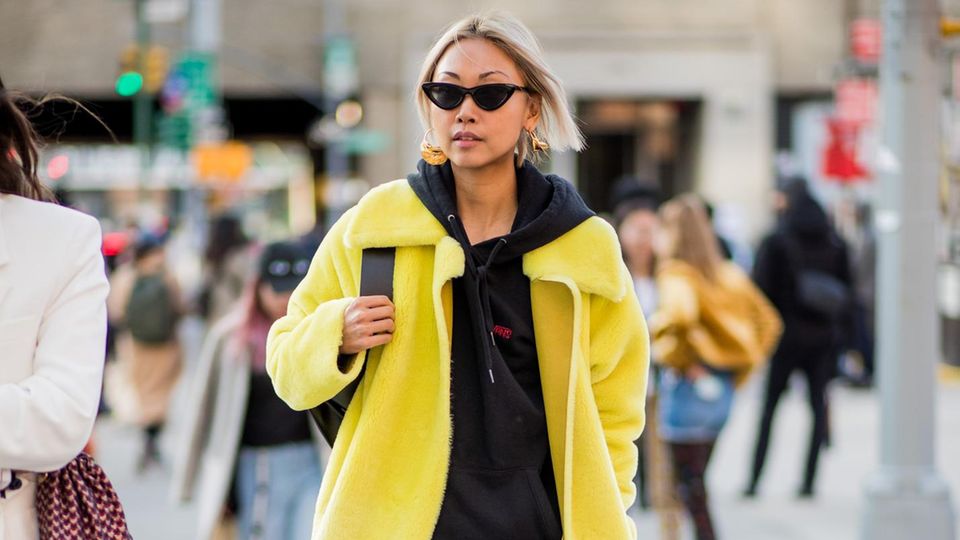 Ein schlichter, lässiger Look. Jeans und Hoodie – doch durch die Kombination mit einem gelben Mantel super schick! 